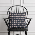 Black and pink patterned pillow on a black chair against a white paneled wall.