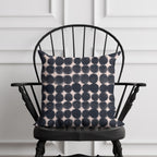 Black and pink patterned pillow on a black chair against a white paneled wall.