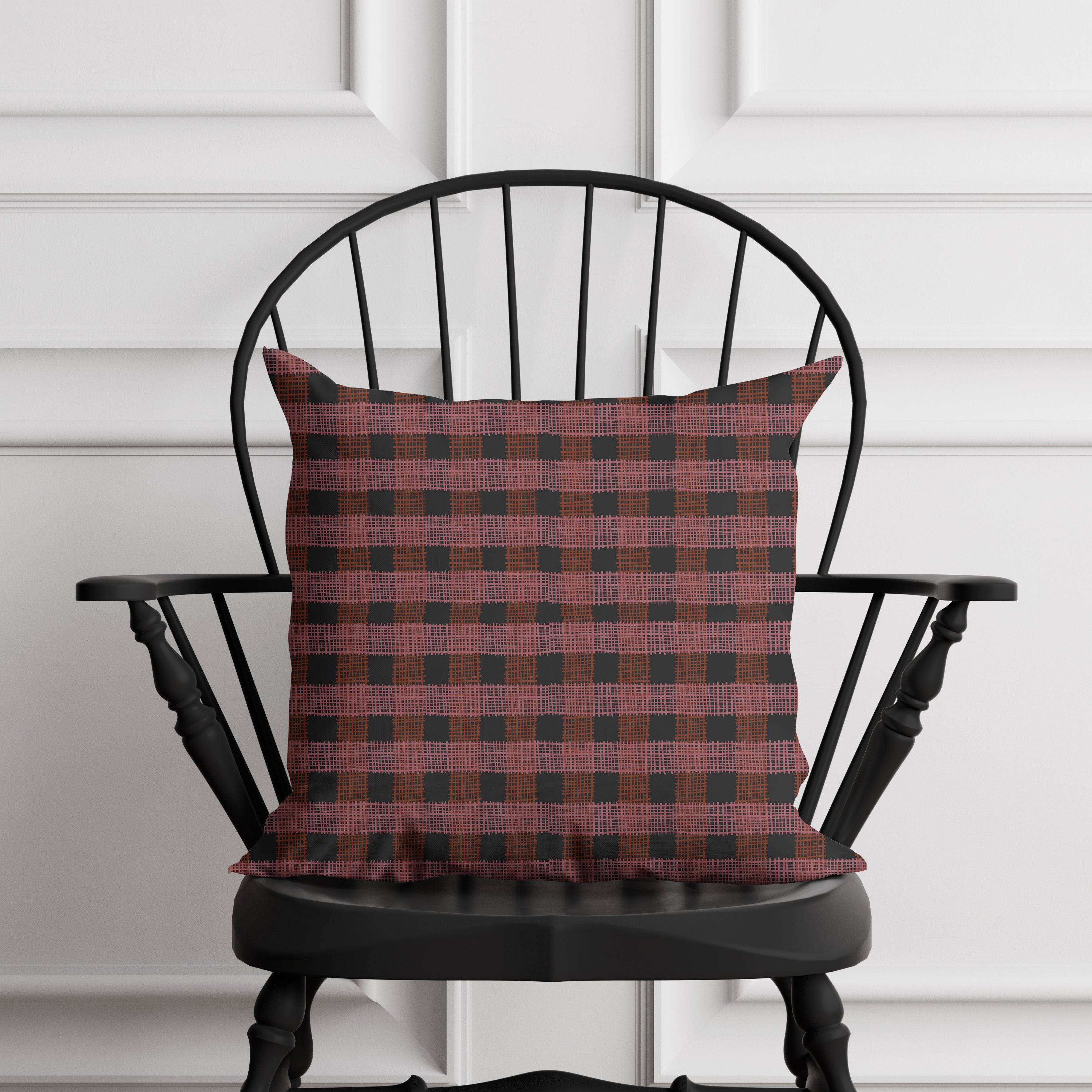 Red and black checkered pillow on a black chair against a white paneled wall.
