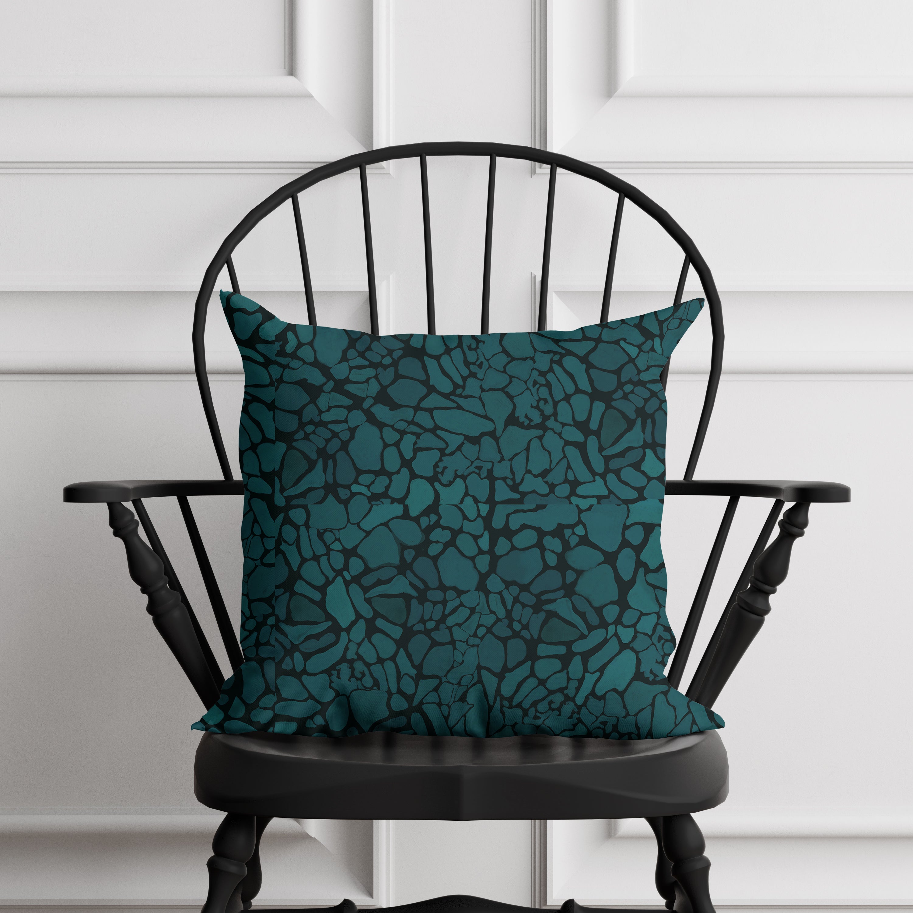 Teal patterned pillow on a black chair against a white paneled wall